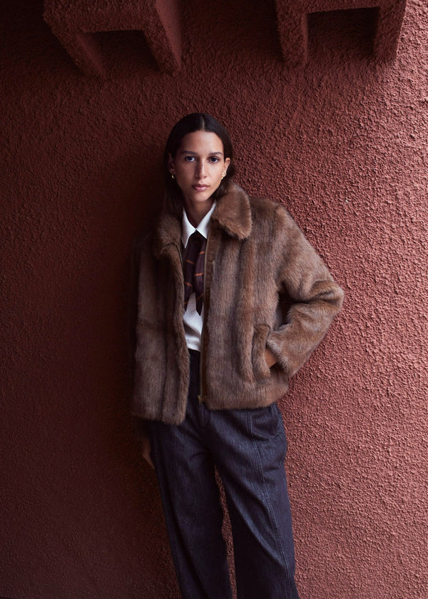 Person wearing a brown fur coat against a textured pink wall
