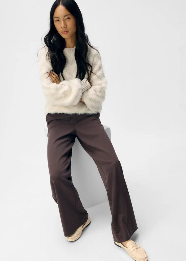 Woman wearing a white sweater and brown pants on a white background