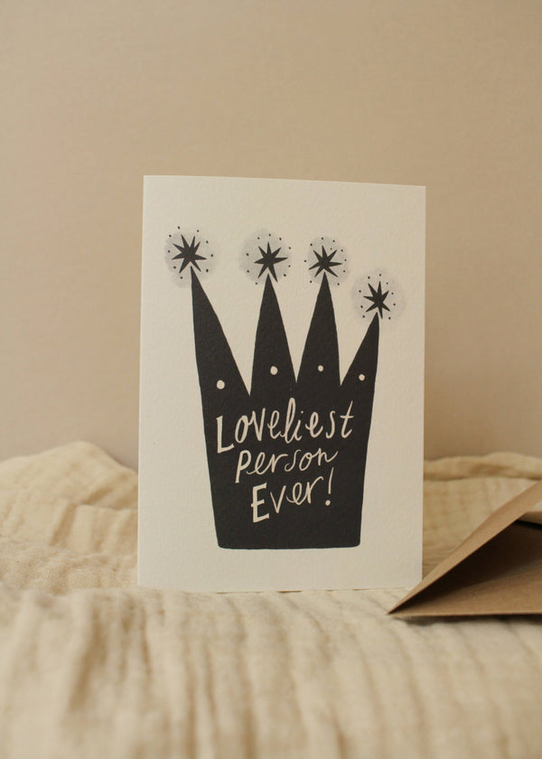 Greeting card with black crown illustration and 'Loveliest Person Ever!' text on a beige background