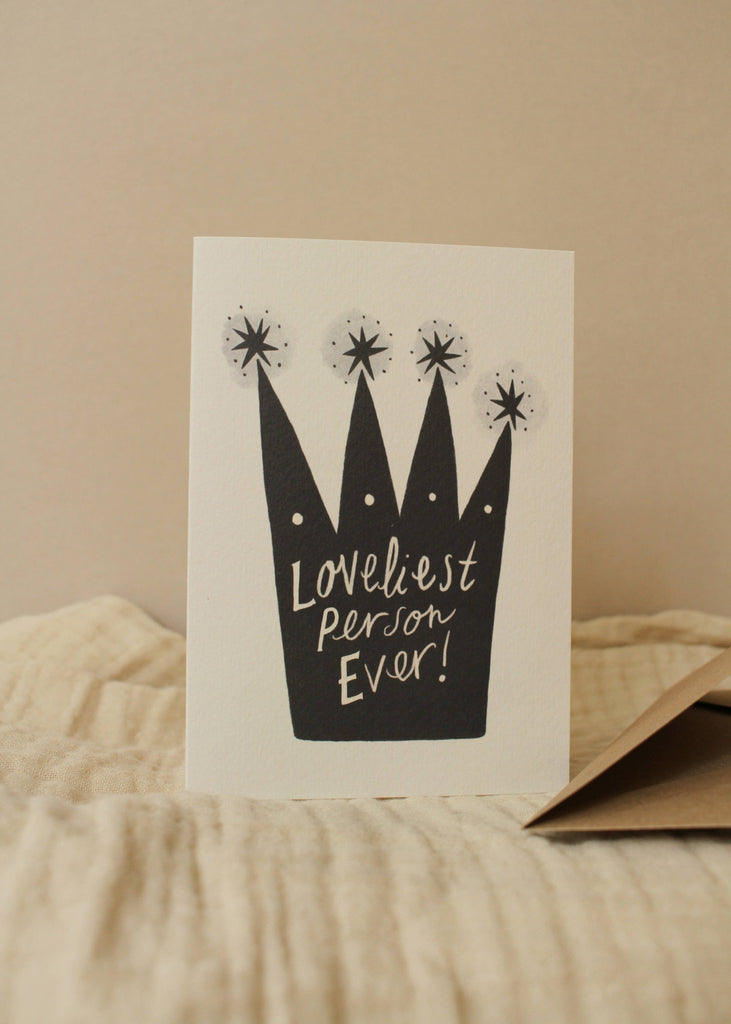 Greeting card with black crown illustration and 'Loveliest Person Ever!' text on a beige background