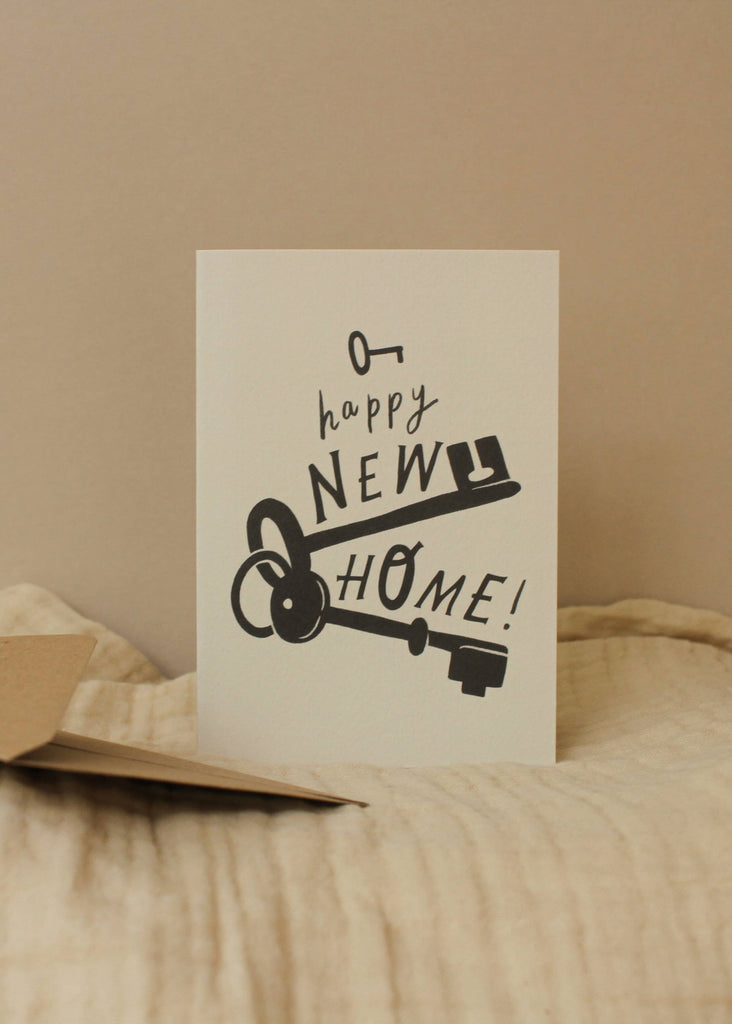 Card with 'Happy New Home!' text and keys on a beige surface
