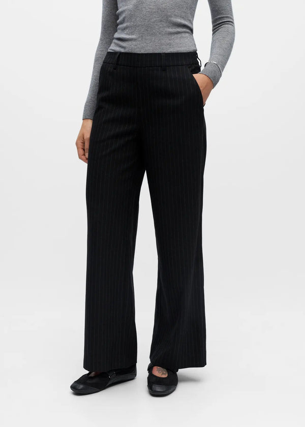 Person wearing black wide-leg pants and a gray top on a white background