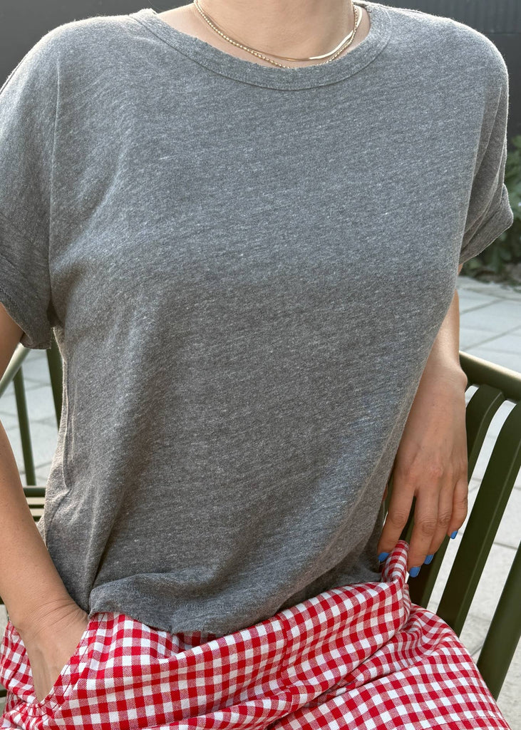 Person wearing a gray t-shirt and red checkered shorts sitting on a chair.