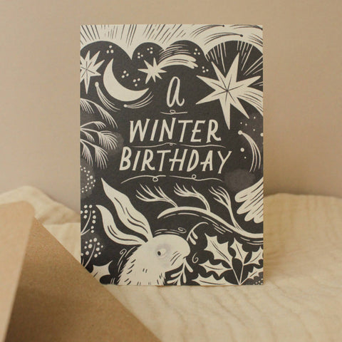 Greeting card with 'A Winter Birthday' text and winter-themed illustrations on a beige background.