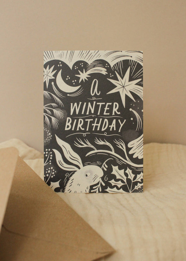 Greeting card with 'A Winter Birthday' text and winter-themed illustrations on a beige background.