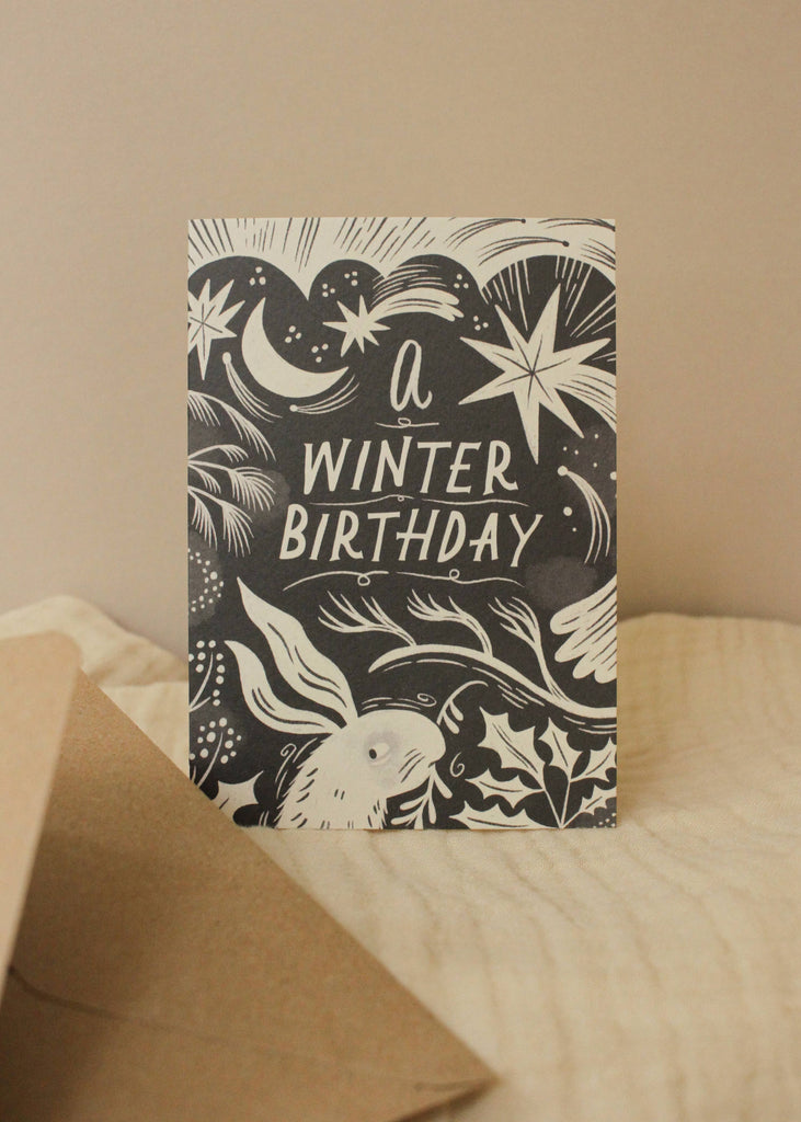 Greeting card with 'A Winter Birthday' text and winter-themed illustrations on a beige background.