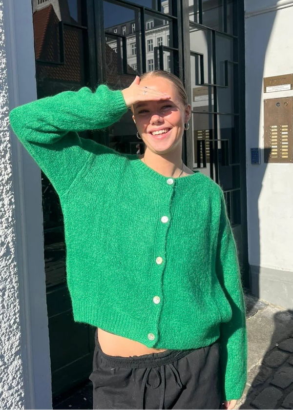 Person wearing a green cardigan standing outdoors near a building entrance.