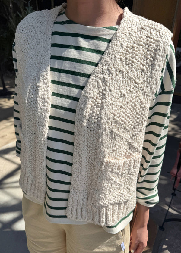 Person wearing a textured cardigan over a striped shirt with beige pants.