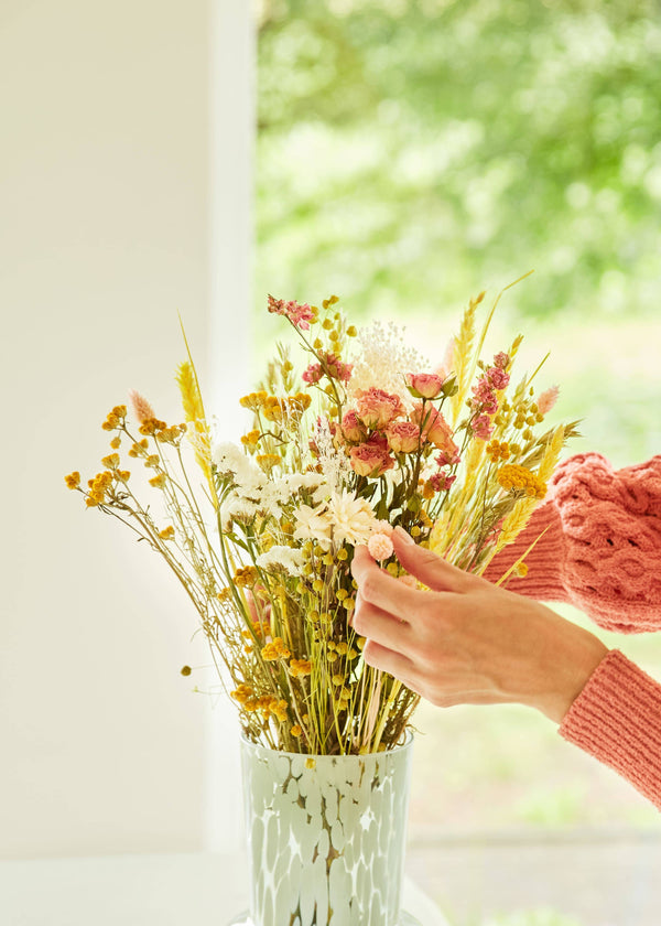 Person arranging flowers in a vase with a blurred green outdoor background