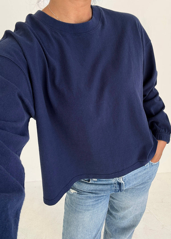 Person wearing a navy blue sweatshirt and light blue jeans on a plain background