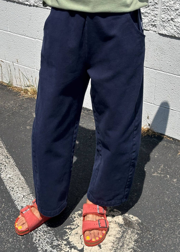 Person wearing navy pants and red sandals standing on a paved surface with a gray wall in the background.