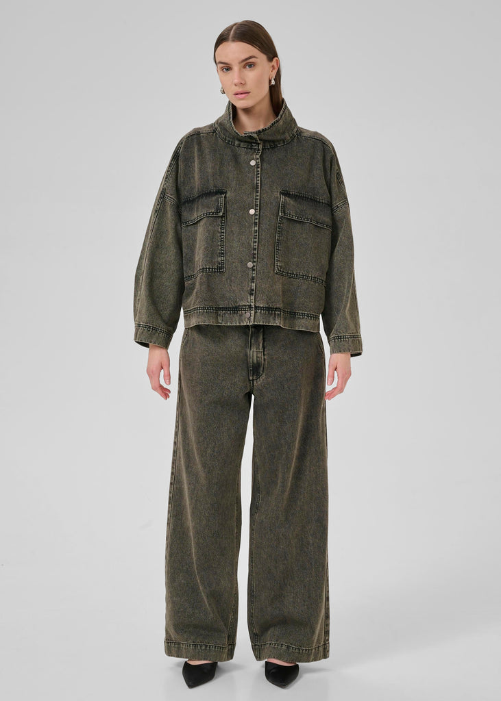Person wearing a green denim jacket and wide-leg jeans on a white background