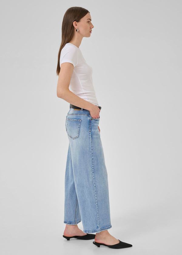 Woman wearing a white t-shirt and light blue jeans on a plain background
