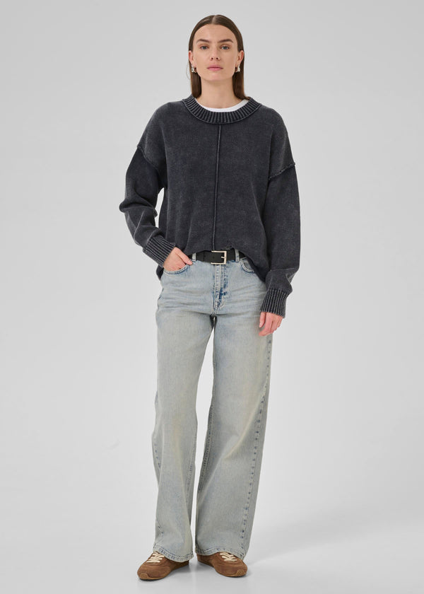 Person wearing a dark gray sweater and light blue jeans on a white background