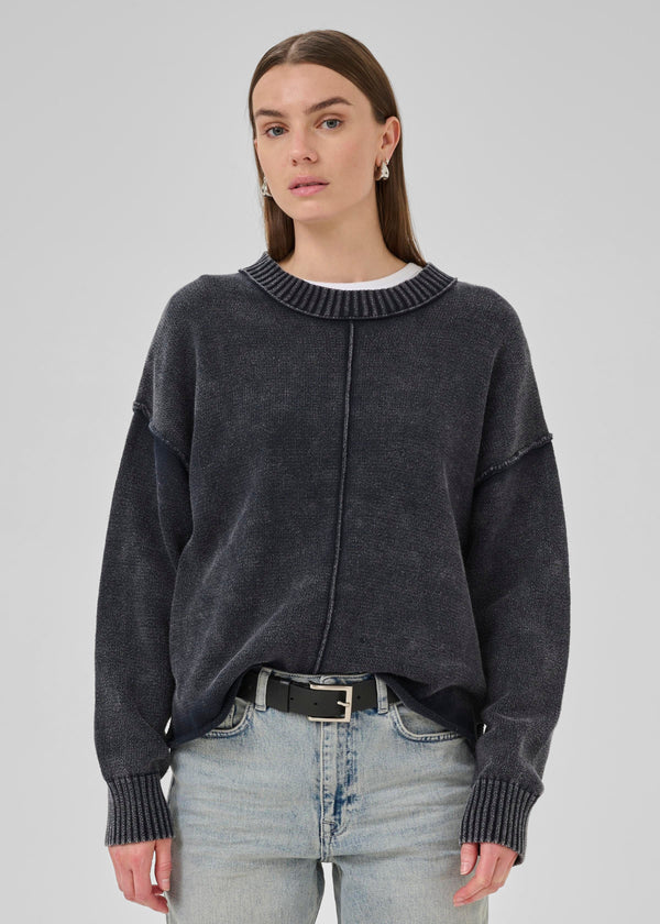 Woman wearing a dark gray sweater and light blue jeans on a plain background