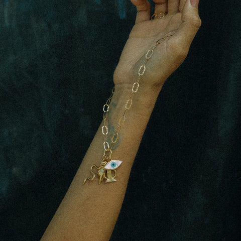 Gold bracelet with a charm on a wrist against a dark background