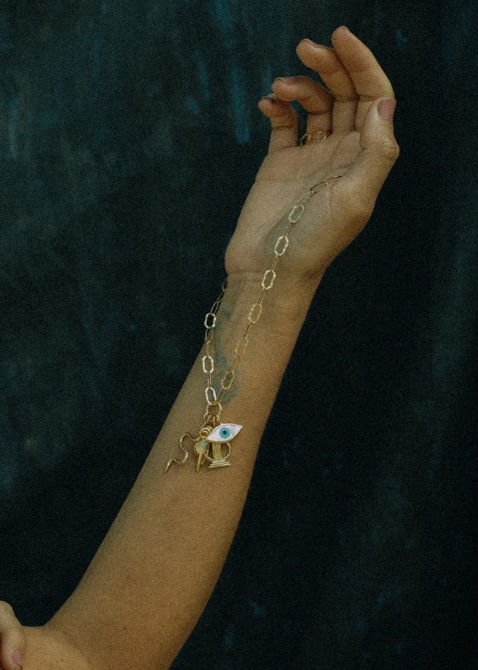 Gold bracelet with a charm on a wrist against a dark background