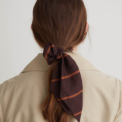 Person wearing a brown striped hair scarf in a ponytail against a plain background