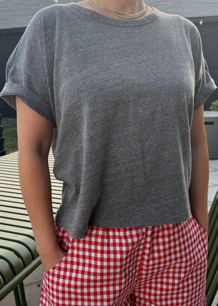 Person wearing a gray t-shirt and red checkered pants outdoors.