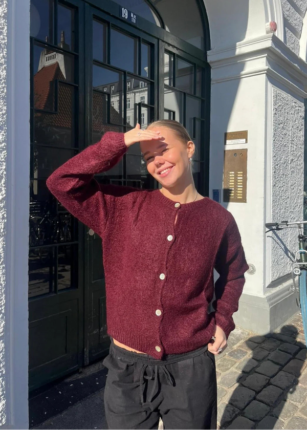 Person wearing a maroon cardigan in front of a building entrance