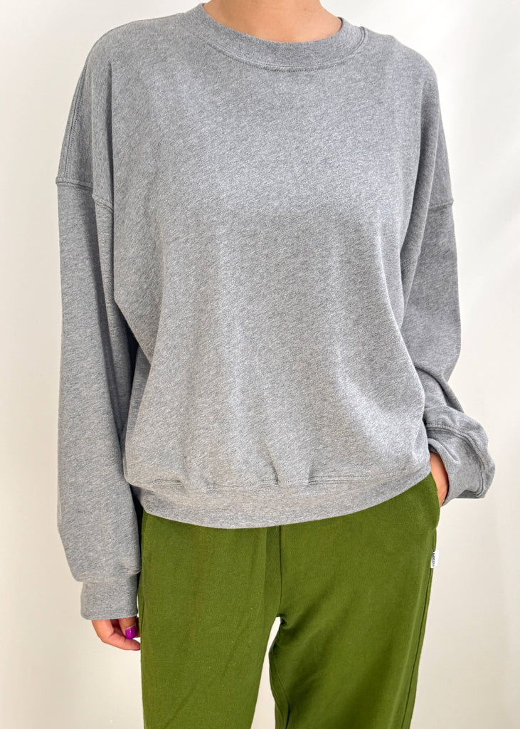 Person wearing a gray sweatshirt and green pants on a plain background