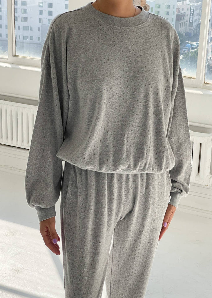 Person wearing a gray lounge set in a room with large windows.