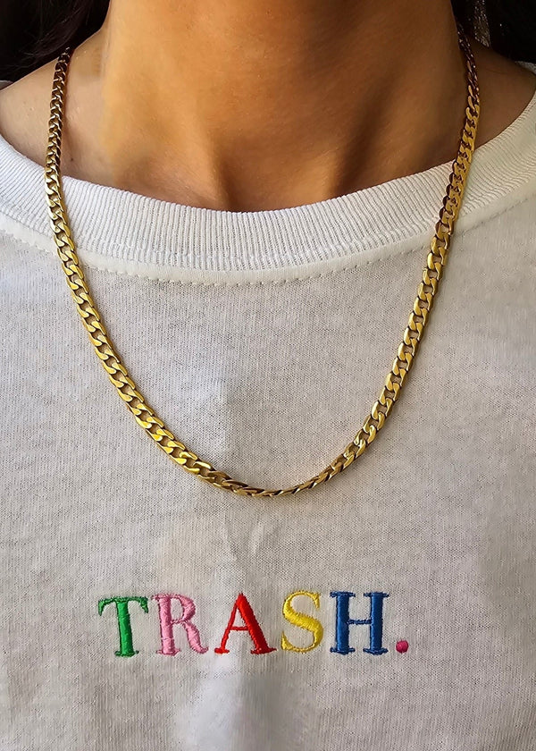 Person wearing a gold chain necklace on a white sweatshirt with 'TRASH' embroidered in colorful letters.