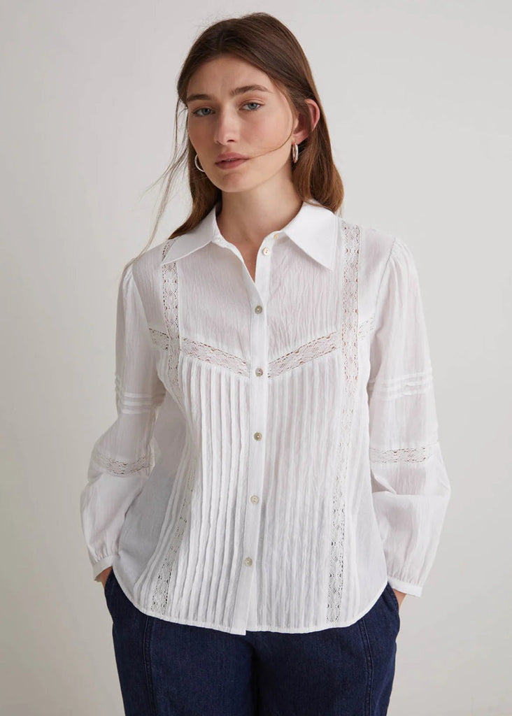 Woman wearing a white blouse with lace details on a plain background