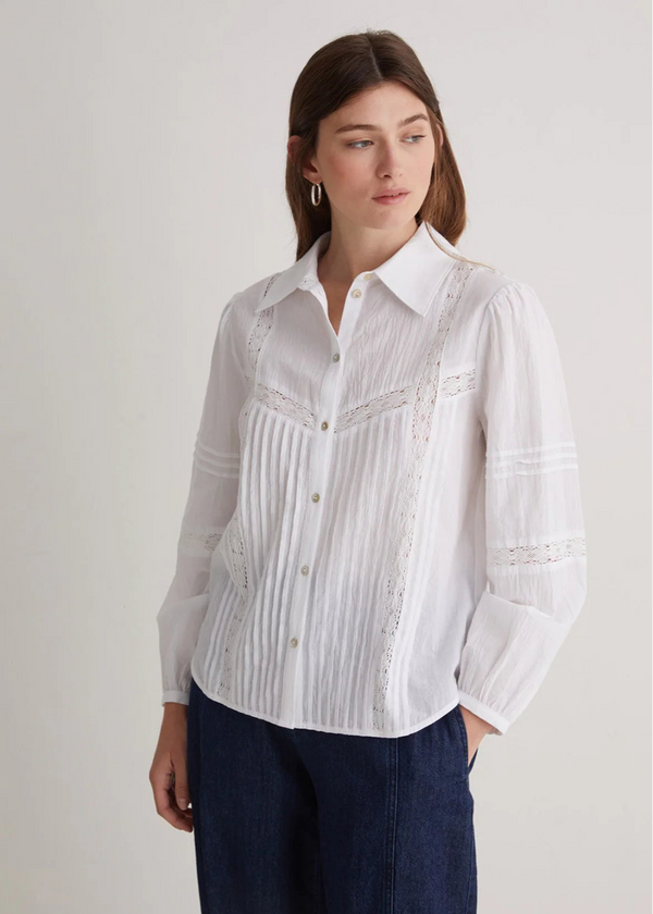 Woman wearing a white button-up shirt with a subtle pattern on a plain background