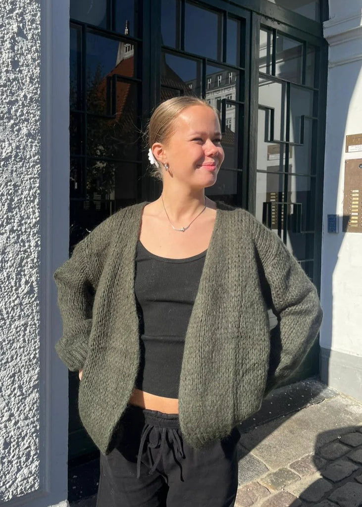 Woman wearing a green cardigan over a black top and pants, standing outside a building.