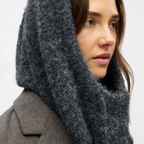 Woman wearing a dark gray hooded scarf against a light background
