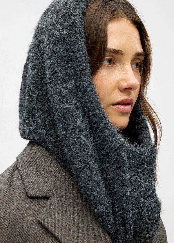 Woman wearing a dark gray hooded scarf against a light background