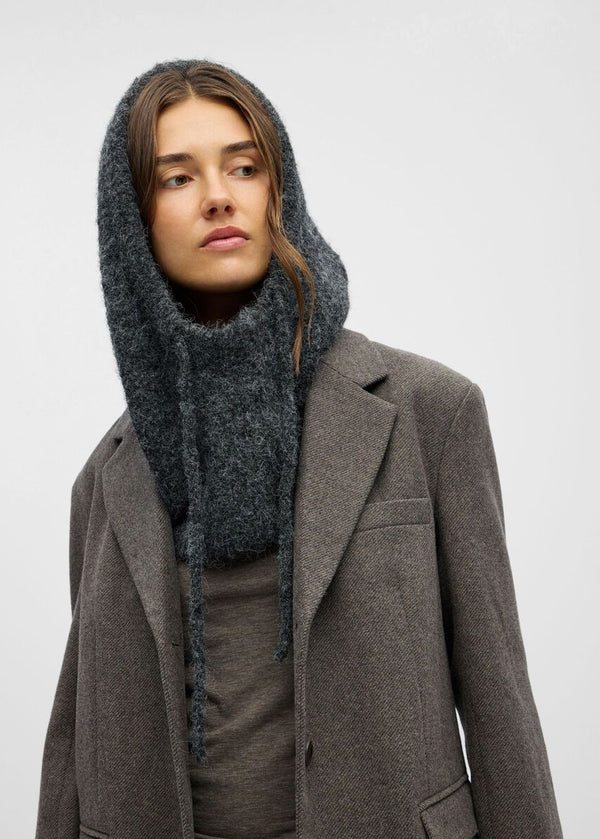 Person wearing a gray coat and hooded scarf on a plain background