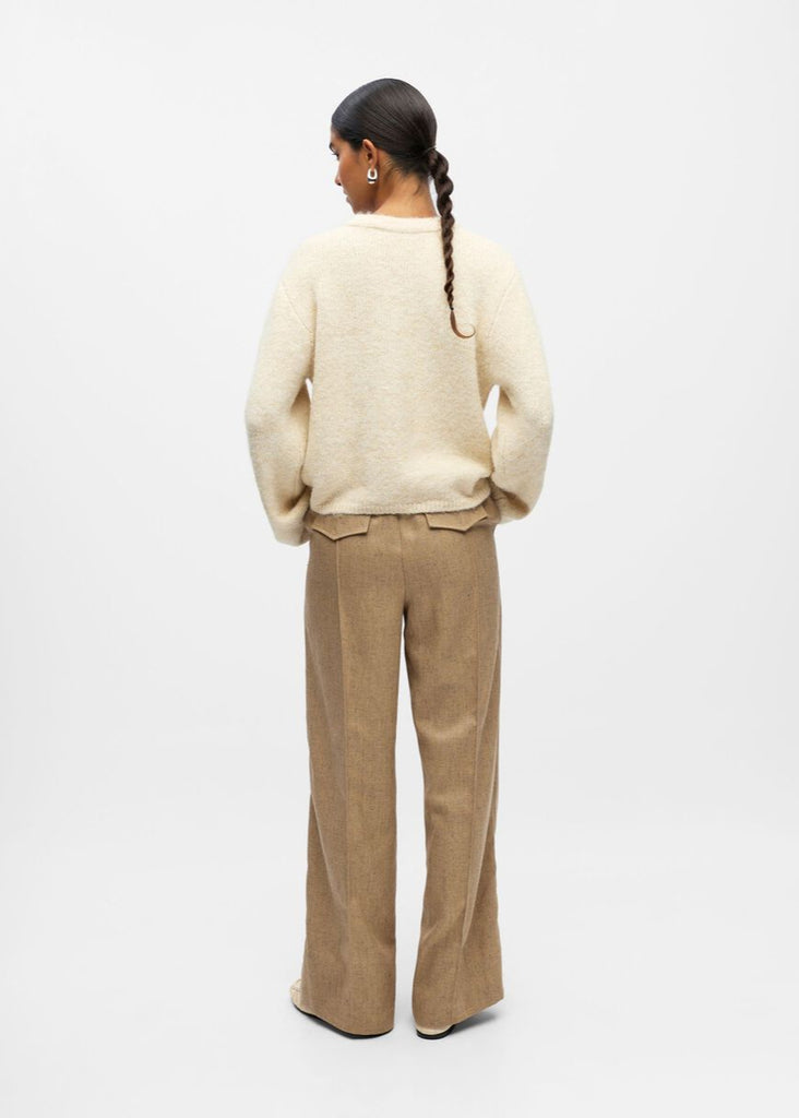 Person wearing a cream sweater and beige pants on a white background