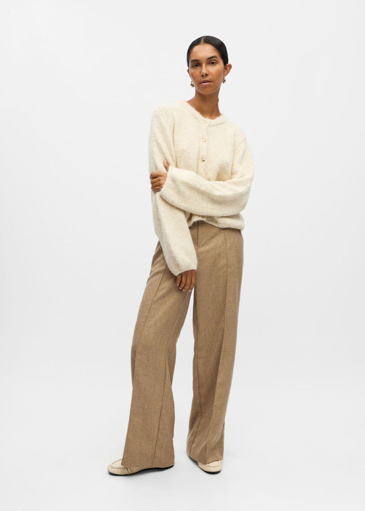 Woman wearing a cream sweater and beige pants on a white background