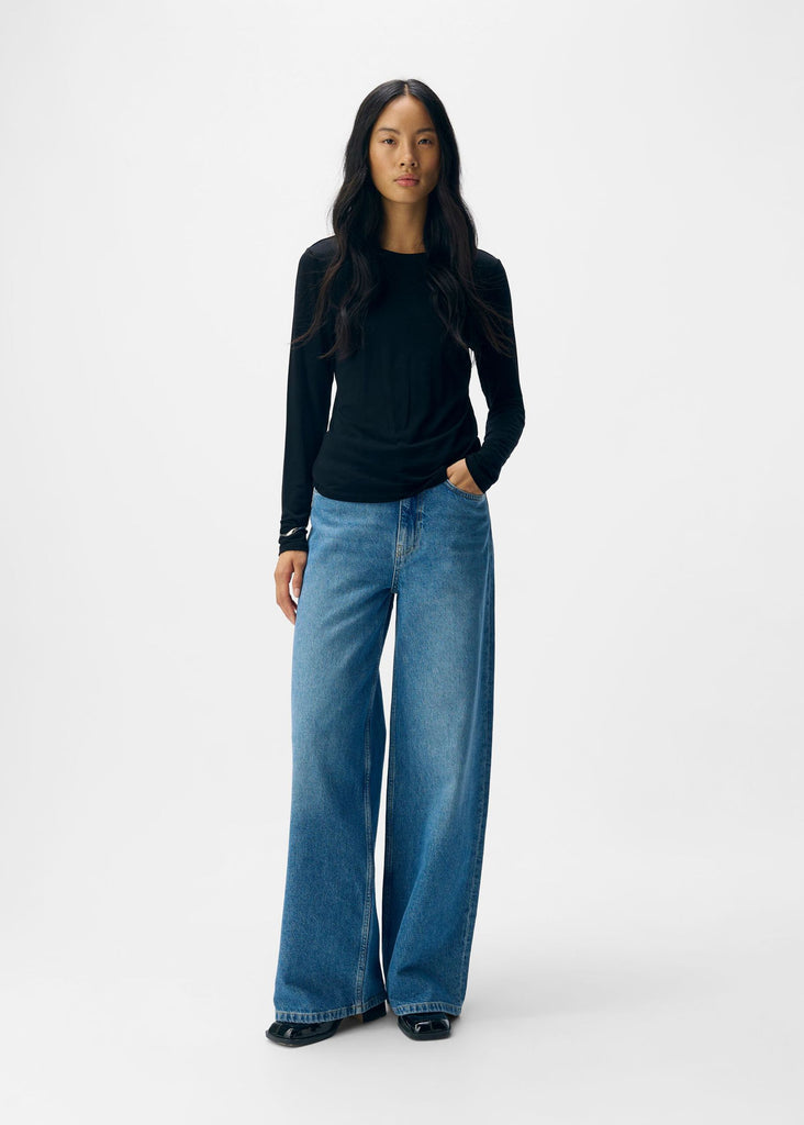 Person wearing a black long-sleeve top and blue jeans on a white background