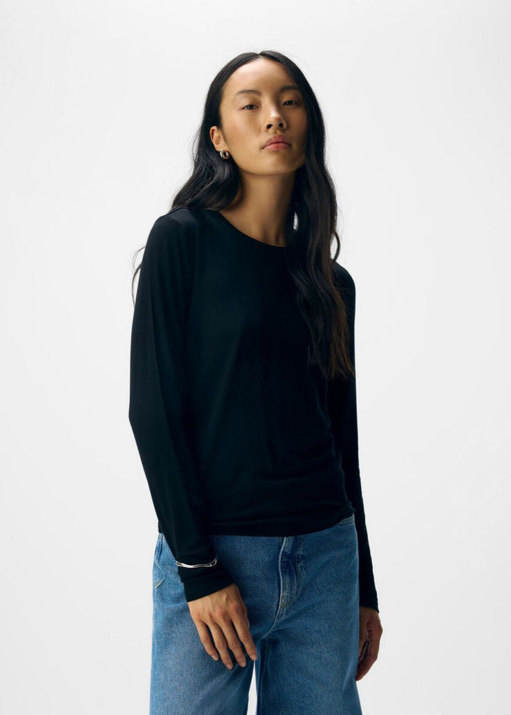 Woman wearing a black long-sleeve top and blue jeans on a white background