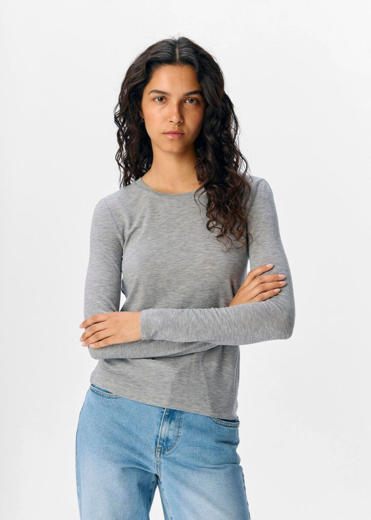 Woman wearing a gray long-sleeve shirt and blue jeans on a white background