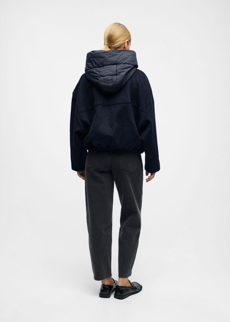 Person wearing a dark blue hooded jacket and pants on a white background