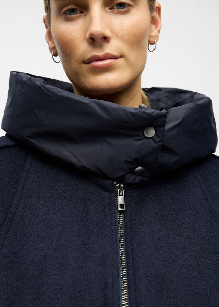 Person wearing a navy blue coat with a high collar on a light gray background