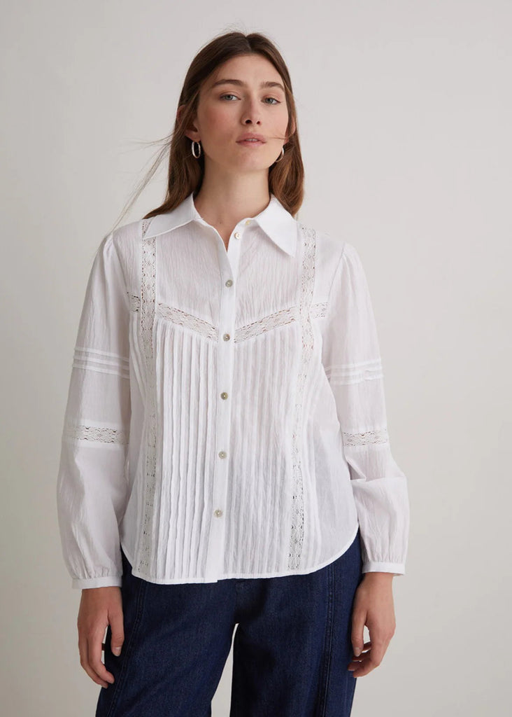 Woman wearing a white embroidered blouse with navy pants on a plain background