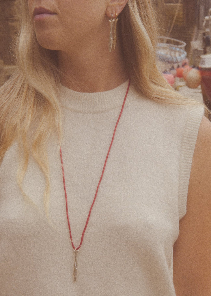 Woman wearing a red necklace with a small pendant, blurred background