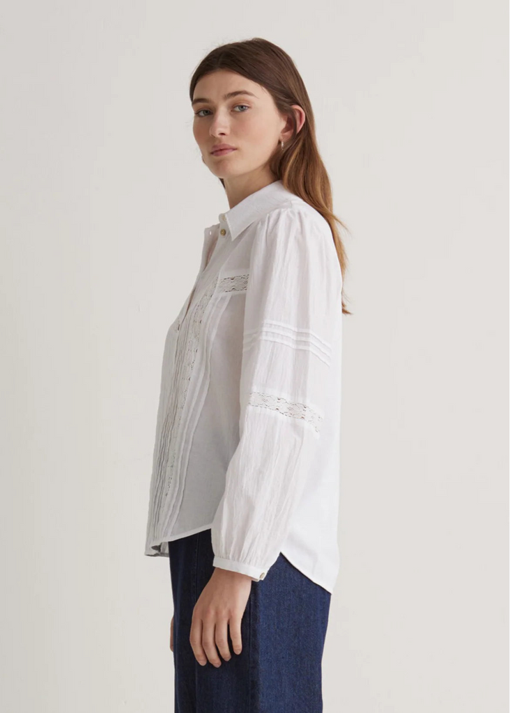Woman wearing a white blouse with a subtle pattern on a plain background