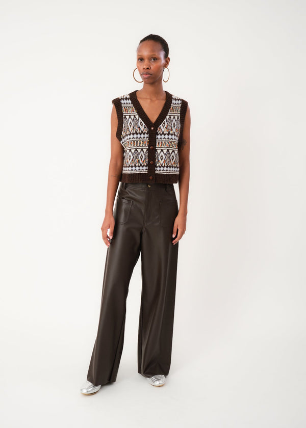 Woman wearing a patterned sleeveless top and black leather pants on a white background