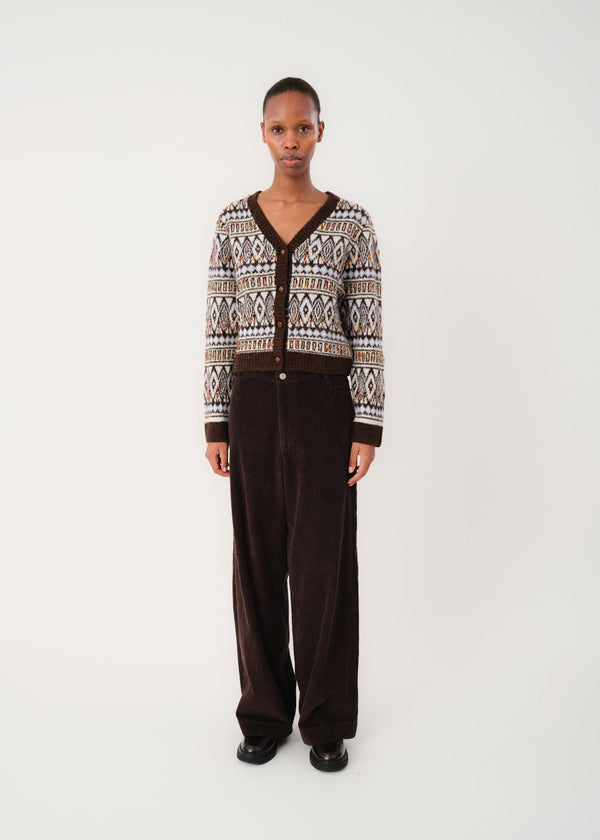 Person wearing a patterned cardigan and dark pants on a white background