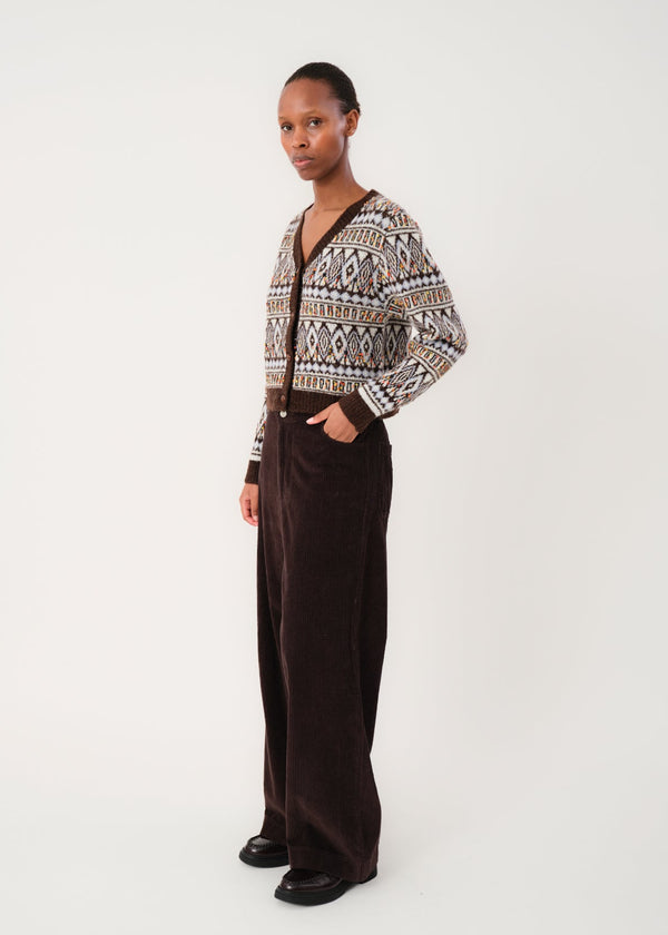 Person wearing a patterned cardigan and brown pants on a white background