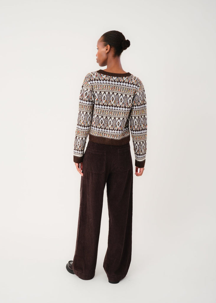 Person wearing a patterned sweater and brown pants on a white background