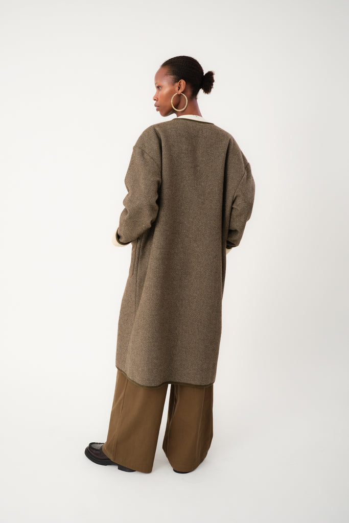 Person wearing a long brown cardigan and pants on a white background