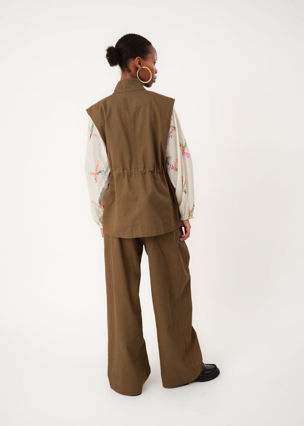 Person wearing a brown vest and pants on a white background