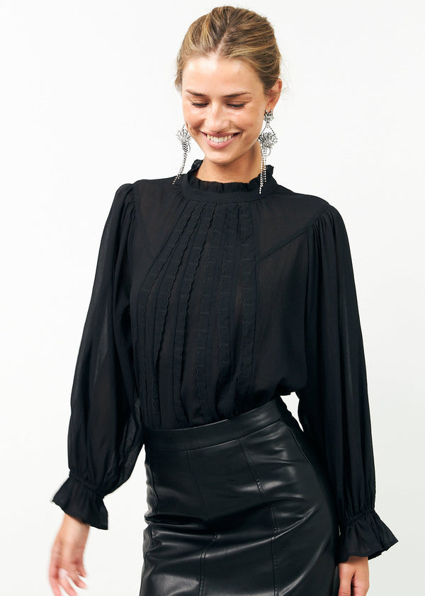 Woman wearing a black blouse with long sleeves and a black leather skirt on a white background